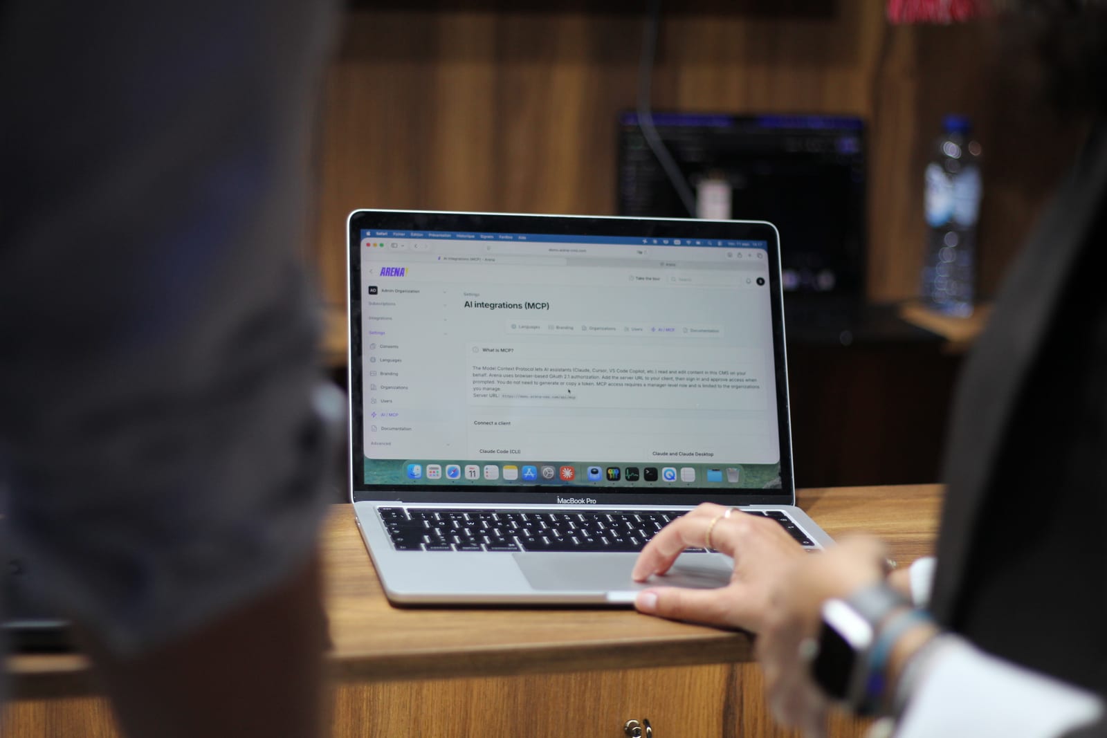 A laptop on the stand showing Arena's AI integrations settings, with the MCP server URL and the options for connecting an AI assistant as a client.